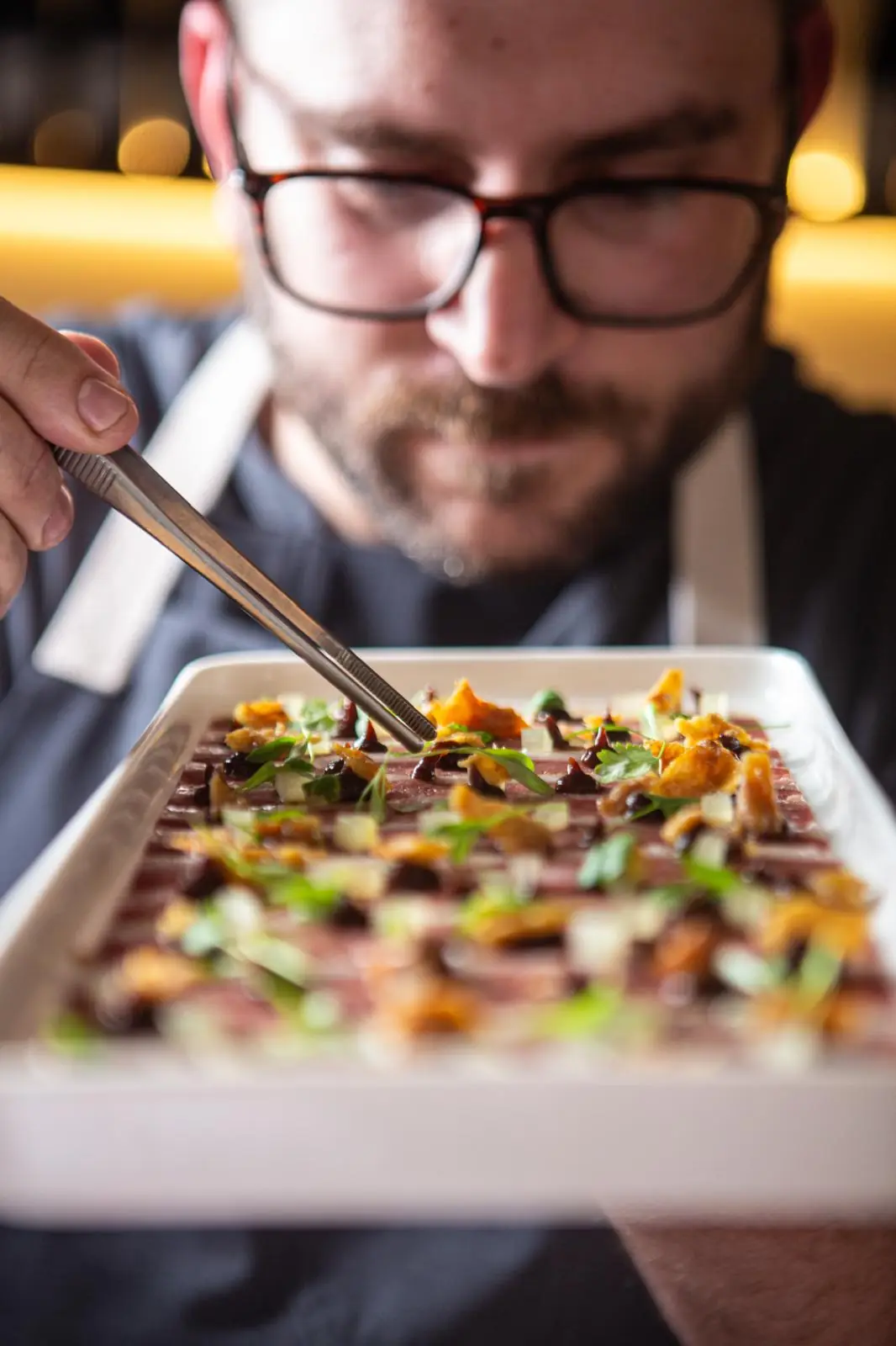 Mans del xef acabant un plat amb herbes fresques a Partager
